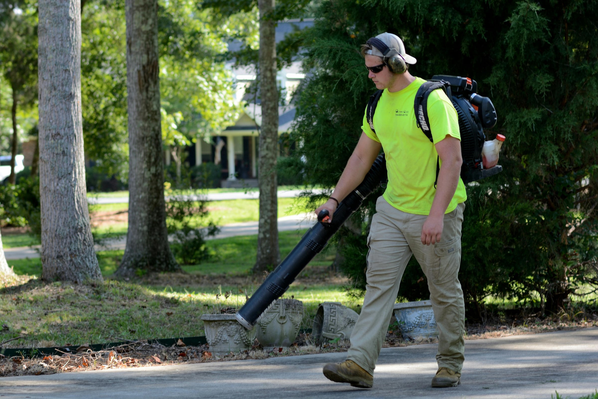 Landscaping worker using a backpack leaf blower on a residential driveway